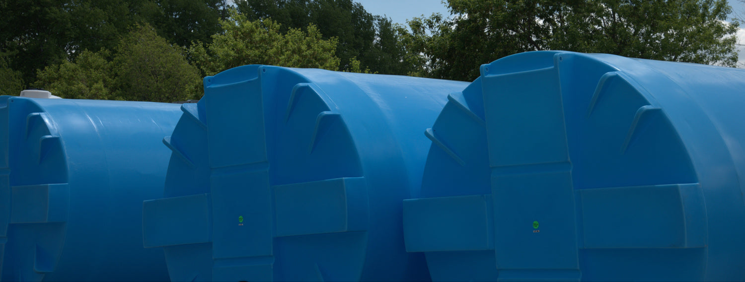 Large blue cylindrical tanks against a backdrop of trees and blue sky with clouds.